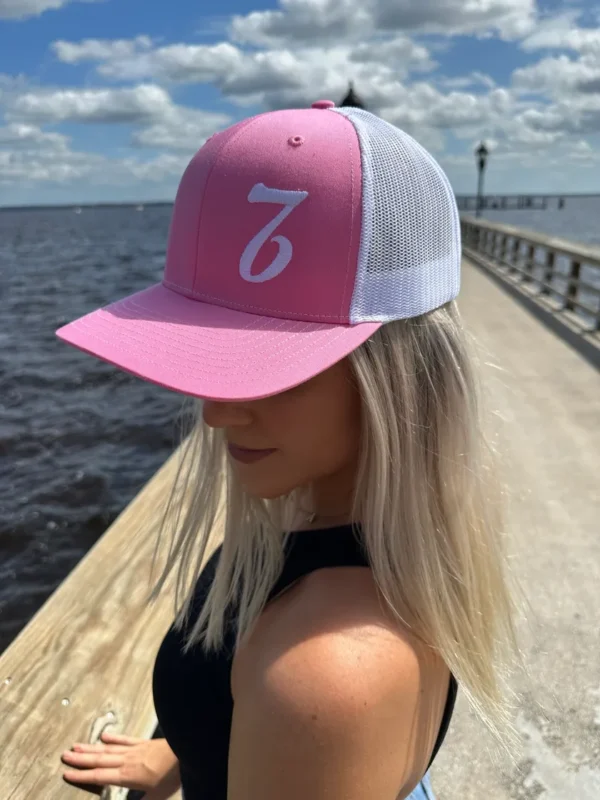 A woman wearing a pink and white hat standing on a pier.