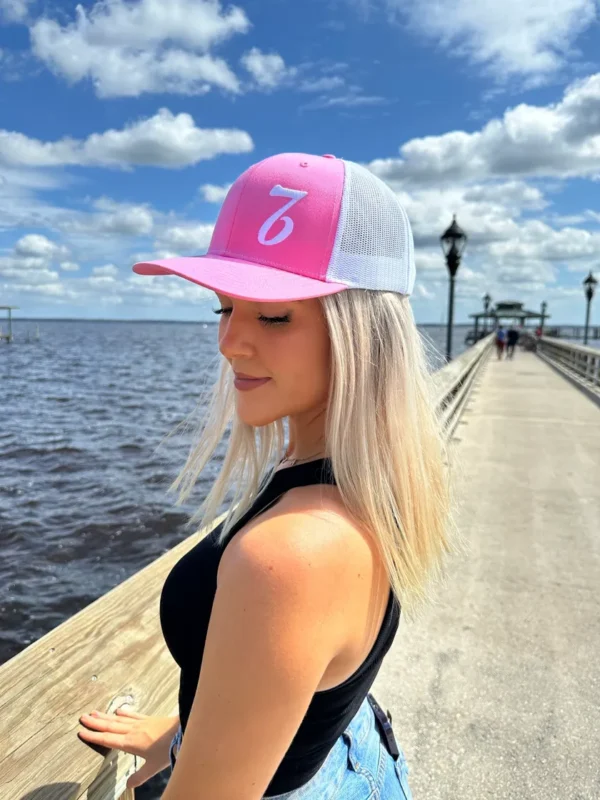 A woman wearing a pink and white hat standing on the pier.